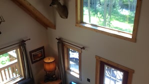 Un interno accogliente con soffitto in legno, una testa di cervo appesa, una poltrona blu, un divano e un tavolo con una lampada.