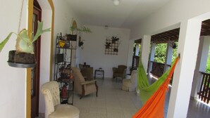 A spacious living area with a hammock, a chair, and a sofa. There are multiple potted plants and a shelf with various items. - ACHIEVING SITE Ground floor, WI FI, Heated pool option, BBQ, Ping Pong (Pinhalzinho)