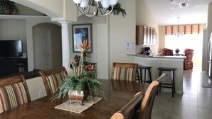 A dining area with a wooden table, chairs, and a potted plant. There is a kitchen in the background with a refrigerator, sink, and countertop. - Renovated Waterfront 4Bd/2Bth Home w/Pool&Spa 20Min to Disney/Shops/Universal (Kissimmee)