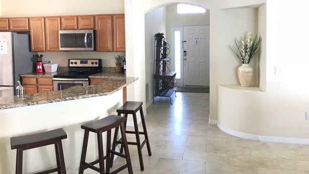 A kitchen with granite countertops, wooden cabinets, a microwave, and a stove. There are two bar stools and a potted plant. - Renovated Waterfront 4Bd/2Bth Home w/Pool&Spa 20Min to Disney/Shops/Universal (Kissimmee)