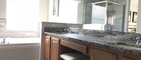 A modern bathroom with a large mirror, granite countertop, wooden cabinets, and a window with patterned curtains.