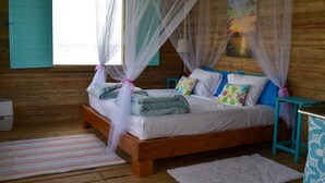 Ein Schlafzimmer einer Holzhütte mit Bett, Moskitonetz und Fenster mit Rollläden.