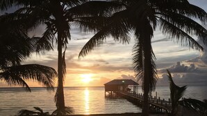 Ein Strand mit einer Holzsteganlage und einer kleinen Konstruktion über dem Wasser bei Sonnenuntergang.