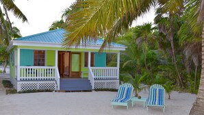 Ein Strandhaus mit Veranda, zwei Liegestühlen und einer Palme im Hintergrund.