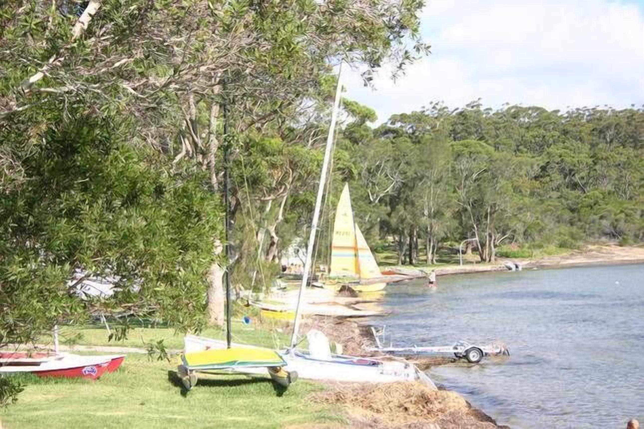 A calm lake with several small sailboats docked along the shore, surrounded by lush greenery.