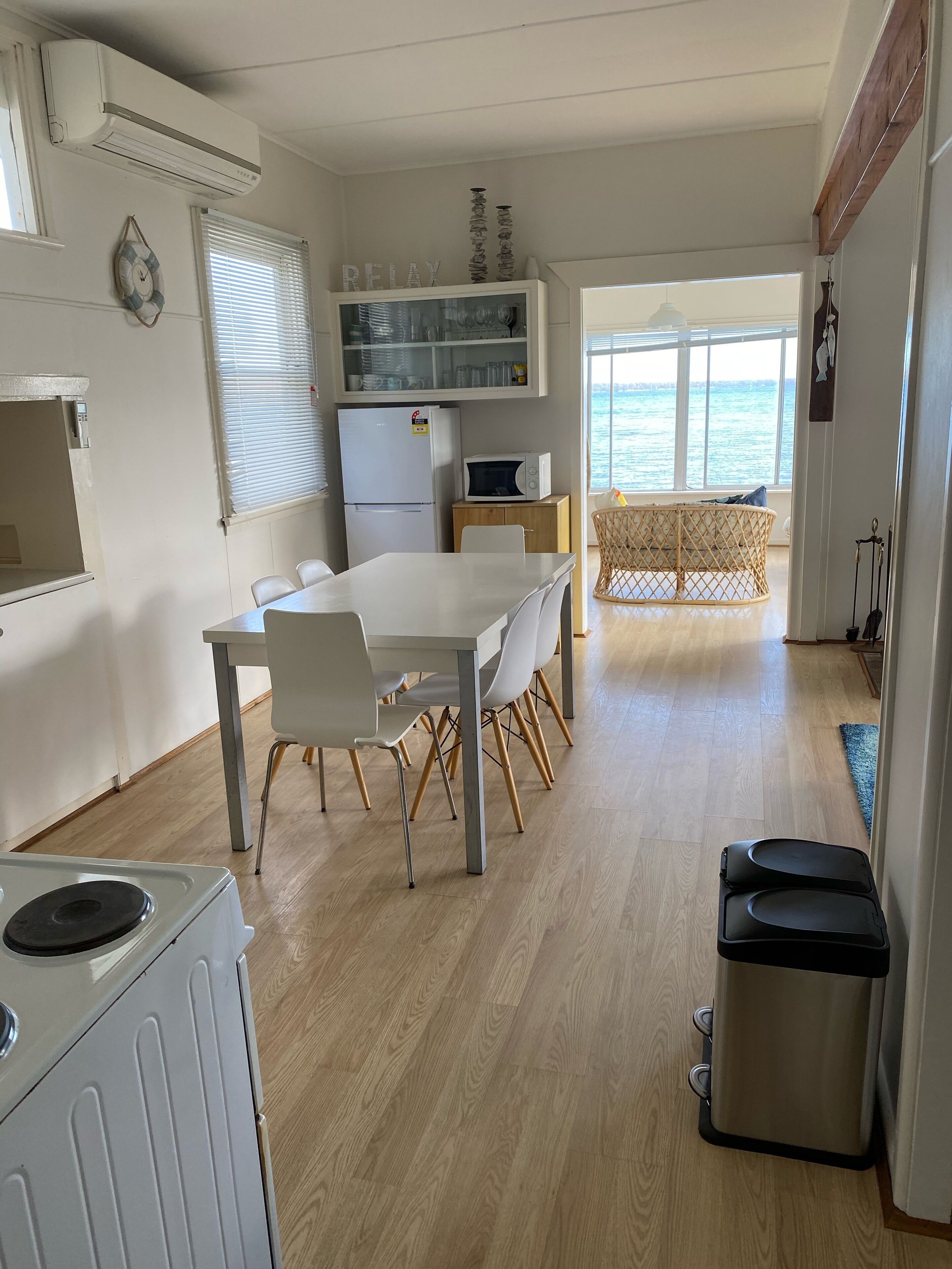 A compact kitchen with a dining area, a microwave, and a refrigerator. There is a view of the sea through large windows.