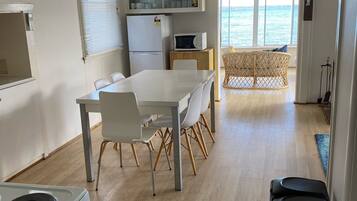 A compact kitchen with a dining area, a microwave, and a refrigerator. There is a view of the sea through large windows.