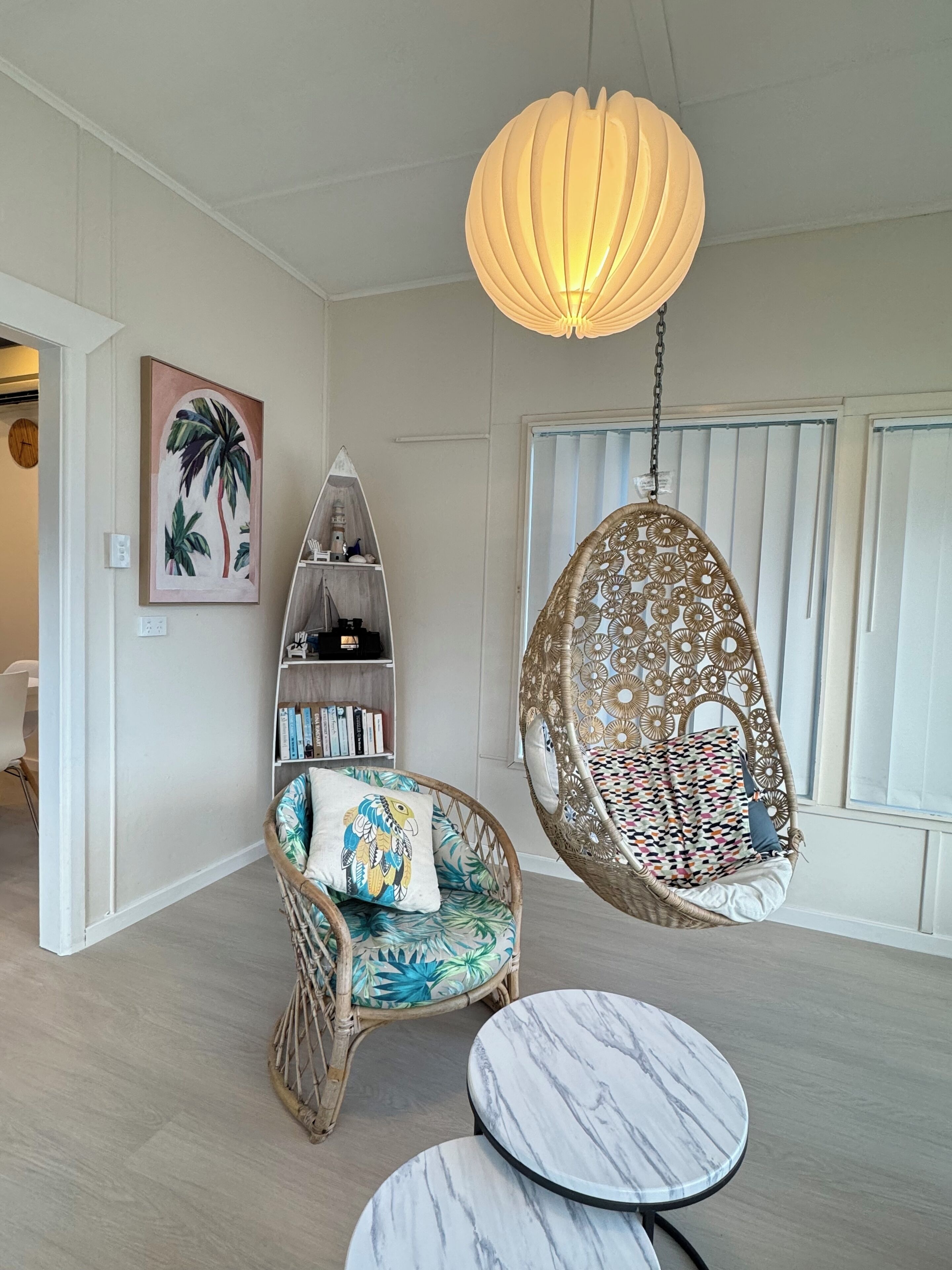 Ein Zimmer mit Hängestuhl, einem runden Tisch, einem Bücherregal und einer großen Leuchte.