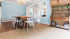 Un coin repas avec une table en bois et des chaises blanches, un lustre et un buffet en bois orné de bols verts.