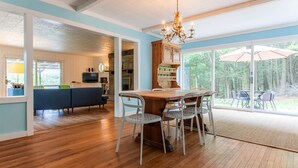 Un vaste espace de vie doté d’un plancher en bois, d’une table à manger avec des chaises, d’un lustre et offrant une vue sur l’extérieur grâce à de grandes fenêtres.