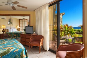 Une chambre d’hôtel avec un balcon, un lit, un bureau avec une télévision et des meubles en osier.