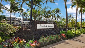 Un letrero con la inscripción '1661 PE E RD' y 'The Makahuena', rodeado de plantas tropicales y palmeras.