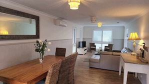 Uma sala de estar ampla com uma mesa de jantar de madeira, cadeiras de vime, um sofá e uma televisão.