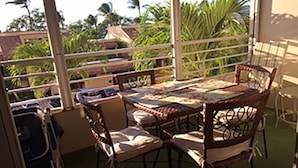 A balcony with a table and chairs, overlooking a garden with palm trees. - Modern, remodeled, ocean views, comfortable and convenient 580 sf (Kihei)