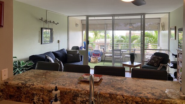 A modern kitchen with a granite countertop, a ceiling fan, and a view of the outdoor patio area. - Modern, remodeled, ocean views, comfortable and convenient 580 sf (Kihei)