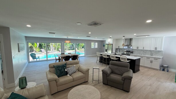 Ampla sala de estar com vista para a piscina, cozinha com armários brancos e espaço de jantar com mesa e cadeiras.