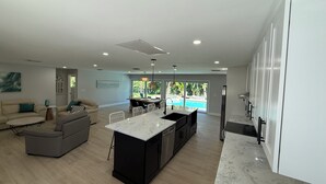 Uma cozinha moderna com uma ilha central, uma sala de jantar com vista para uma piscina e uma sala de estar com sofá e mesa de centro.