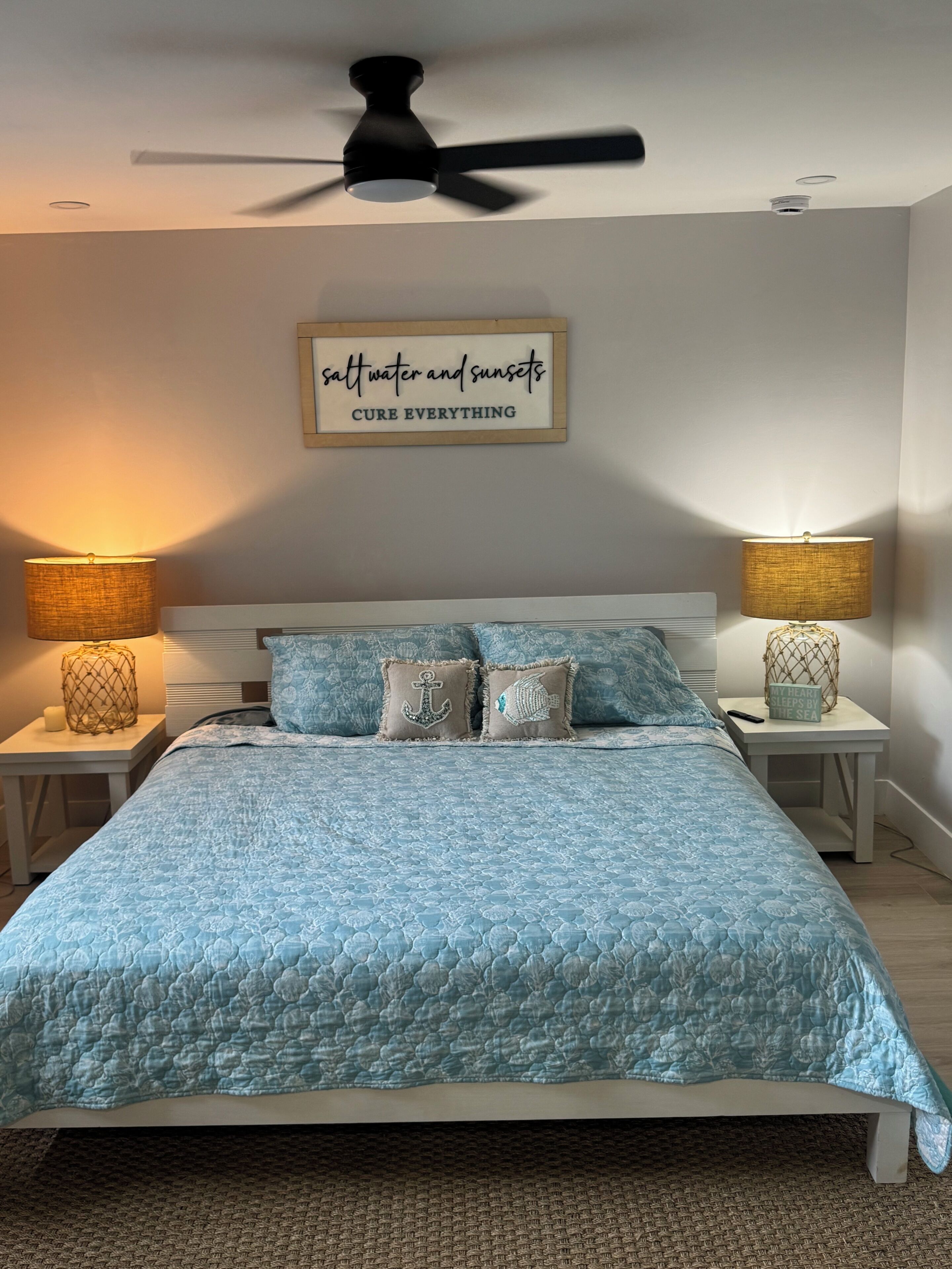 A bedroom with a bed, two nightstands, a ceiling fan, and a wall sign.