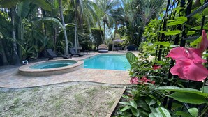 Uma piscina com borda de tijolos, cercada por vegetação exuberante e palmeiras.