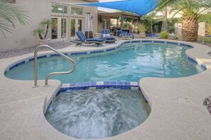 Une piscine avec un jacuzzi, des chaises longues et un patio couvert.