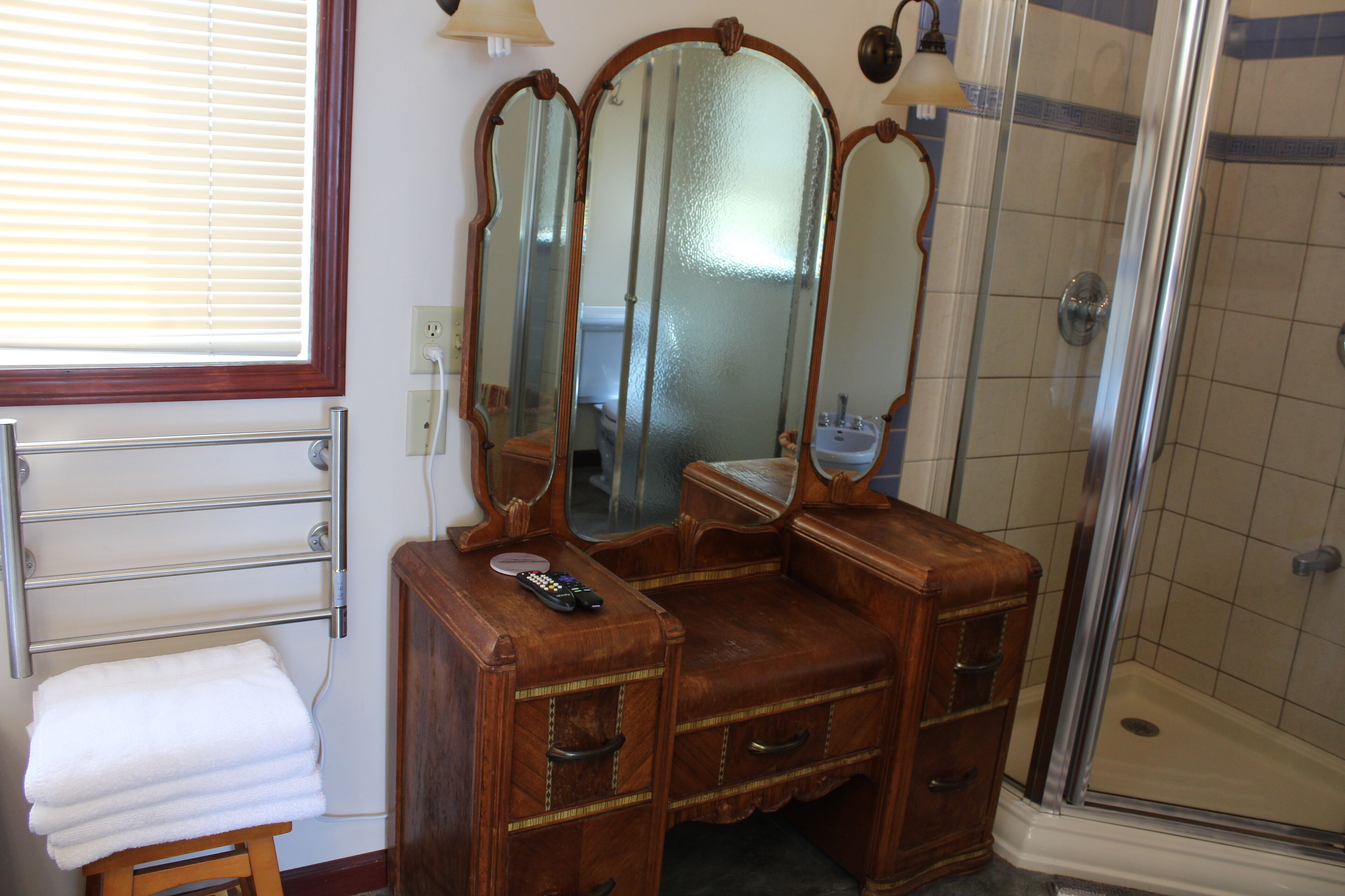 A bathroom with a vanity, a mirror, a shower, and a towel rack.