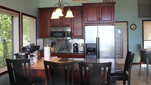 A kitchen with wooden cabinets, stainless steel appliances, and a dining area with a marble countertop and chairs. - BEACHFRONT /HOTTUB/STEAM ROOM/GAME ROOM/JACUZZI/PETS/MASSAGE CHAIR/KAYAKS/BIKES (Michigan City)