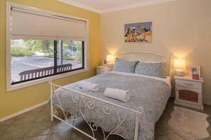 A bedroom with a bed, two bedside tables, a window with a view, and a painting on the wall.