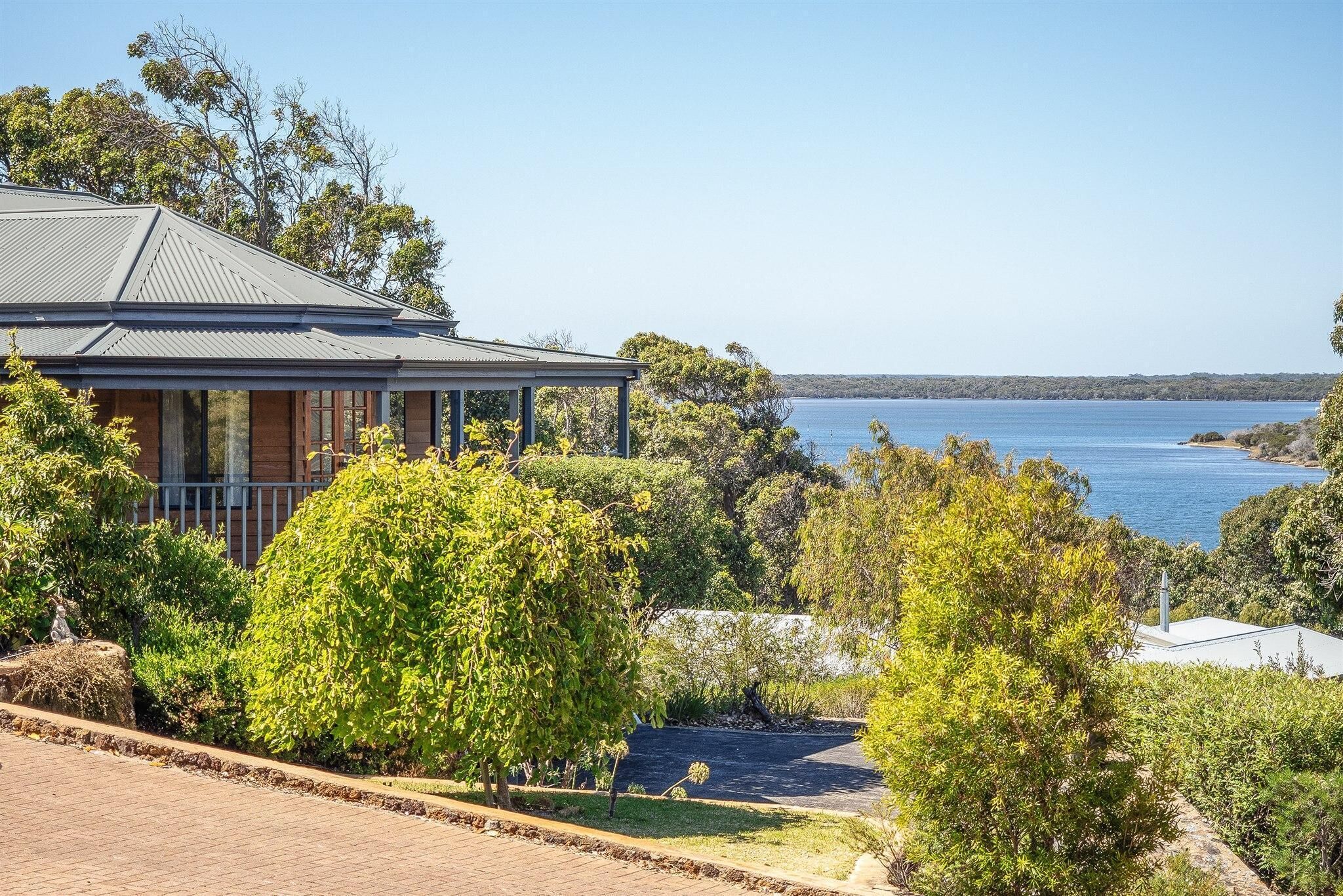 A house with a view of a lake, surrounded by trees and a paved driveway.