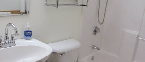 A bathroom with a sink, toilet, and bathtub. There is a shelf above the toilet and a showerhead above the bathtub.