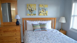 Une chambre à coucher avec un lit en bois, deux oreillers, une commode, un miroir et deux tableaux accrochés au mur.