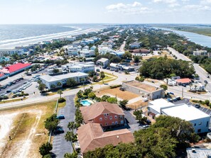 Ein Luftbild einer Küstenstadt mit Strand, Wohnhäusern und einem großen Hotel mit Schwimmbad.