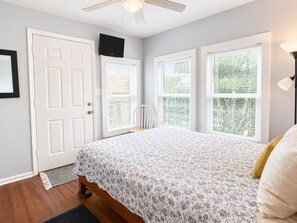 Une chambre à coucher avec un lit, un ventilateur de plafond, une porte et des fenêtres équipées de stores.