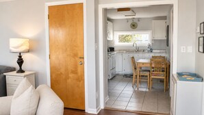 Une pièce avec une porte en bois, une table à manger avec des chaises, un coin cuisine avec des placards et une lampe sur une table de chevet.