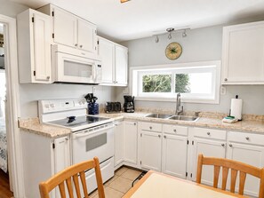 Une cuisine avec des meubles blancs, un four à micro-ondes, une cuisinière, un grille-pain et une fenêtre donnant sur un paysage verdoyant.