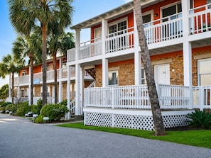 A multi-story residential building with balconies, brick facade, and palm trees.