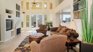 A spacious living room with a large television, comfortable seating, and a decorative plant.