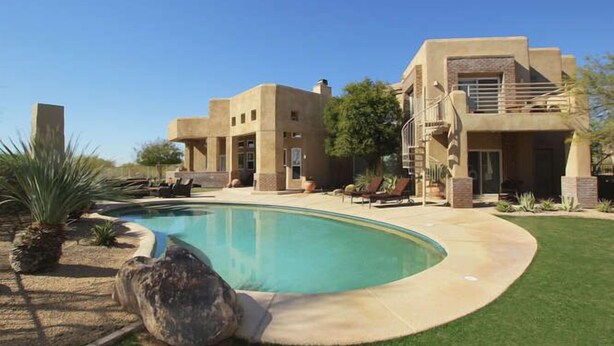 A modern house with a swimming pool, a patio with lounge chairs, and a well-maintained lawn.