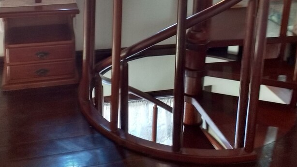Una escalera de madera con barandilla curva, un aparador de madera y una pequeña planta en maceta sobre una mesa.