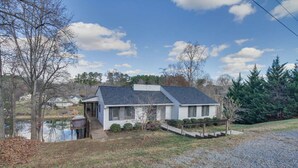 A single-story house with a sloped roof, a small porch, and a pond in the background. - "Sunny Days"-Relaxation for All! Wifi-4 HDTVs-Open/Cov Dock-Game Rm-Linens Incl (Moneta)