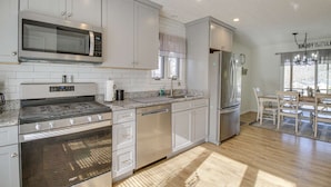 A modern kitchen with white cabinets, stainless steel appliances, and a dining area with a chandelier. - "Sunny Days"-Relaxation for All! Wifi-4 HDTVs-Open/Cov Dock-Game Rm-Linens Incl (Moneta)
