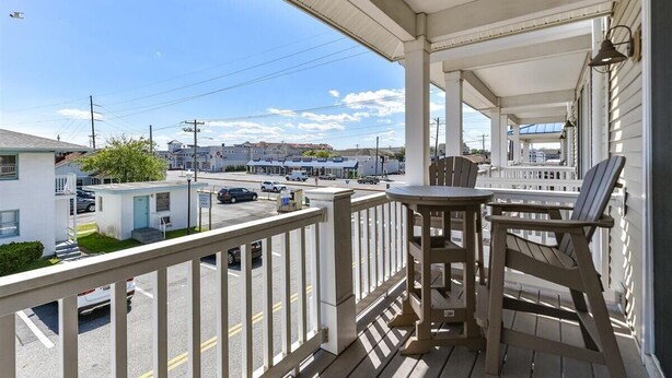 A covered porch with a table and chairs, overlooking a street with buildings and parked cars.