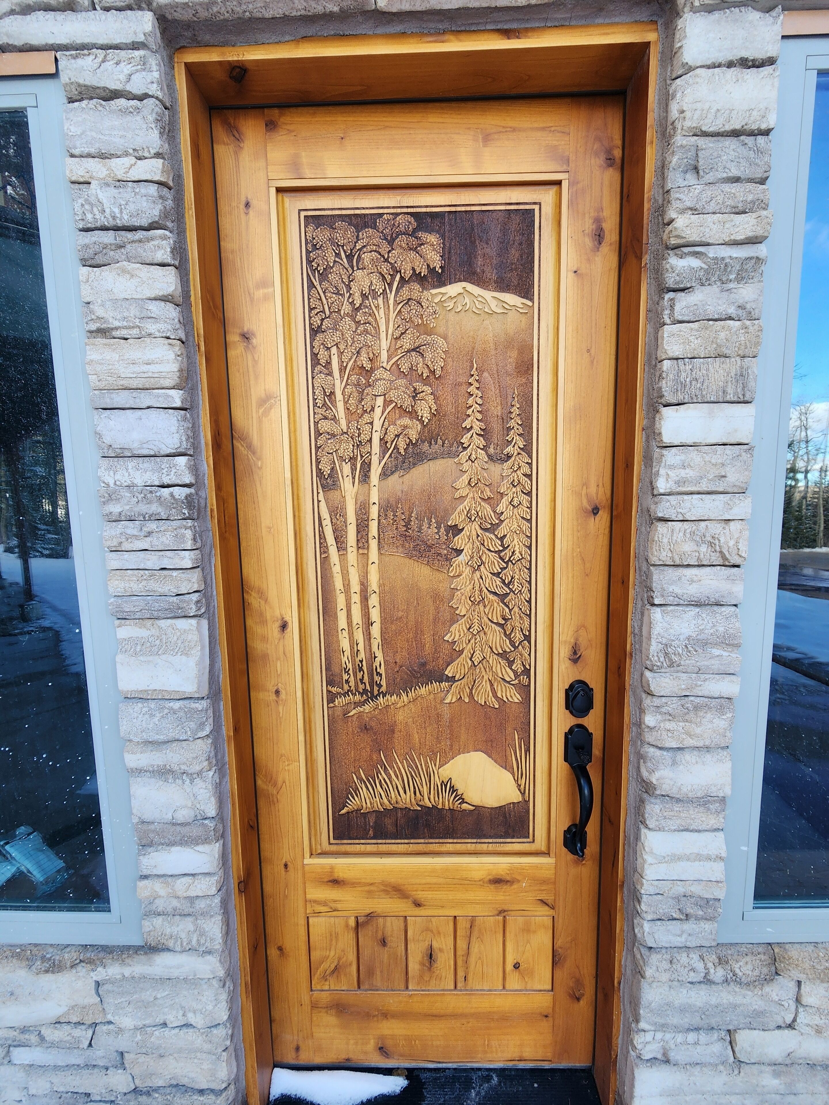 A wooden door with a carved landscape scene, flanked by stone walls and windows.