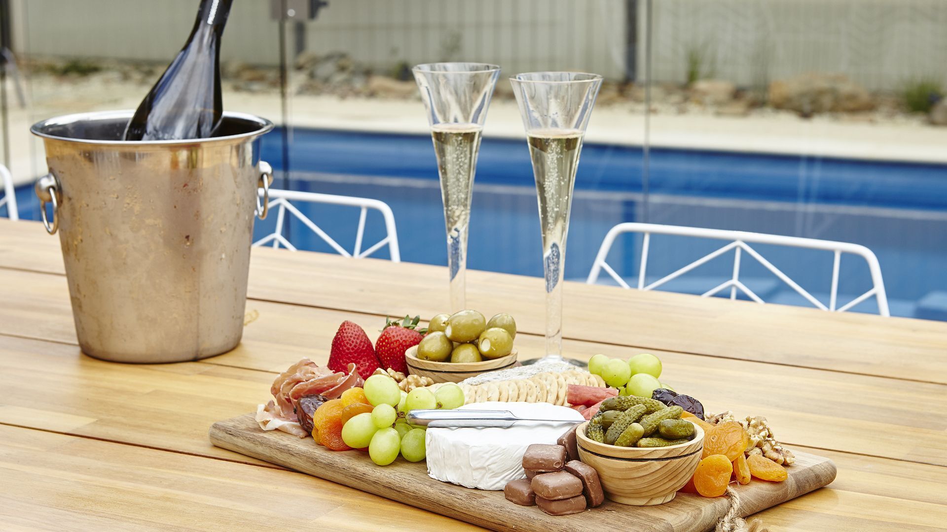 A wooden table with a charcuterie board, two glasses of champagne, and a metal pot.