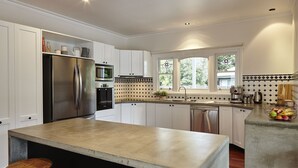 A modern kitchen with white cabinetry, stainless steel appliances, a large island, and a window providing natural light. - Lumley House Bright c1898 (Bright)