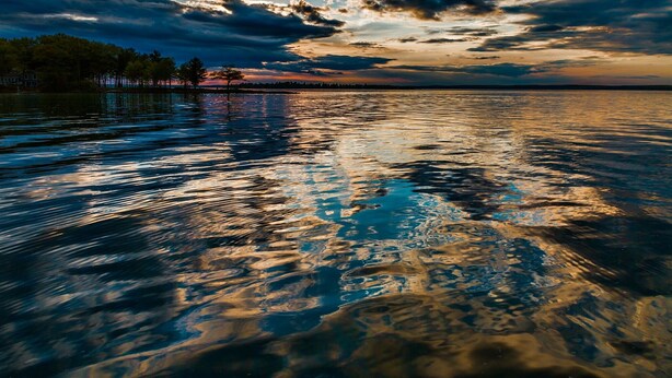 Un lago tranquillo con i riflessi di alberi e di una casa sulla riva.