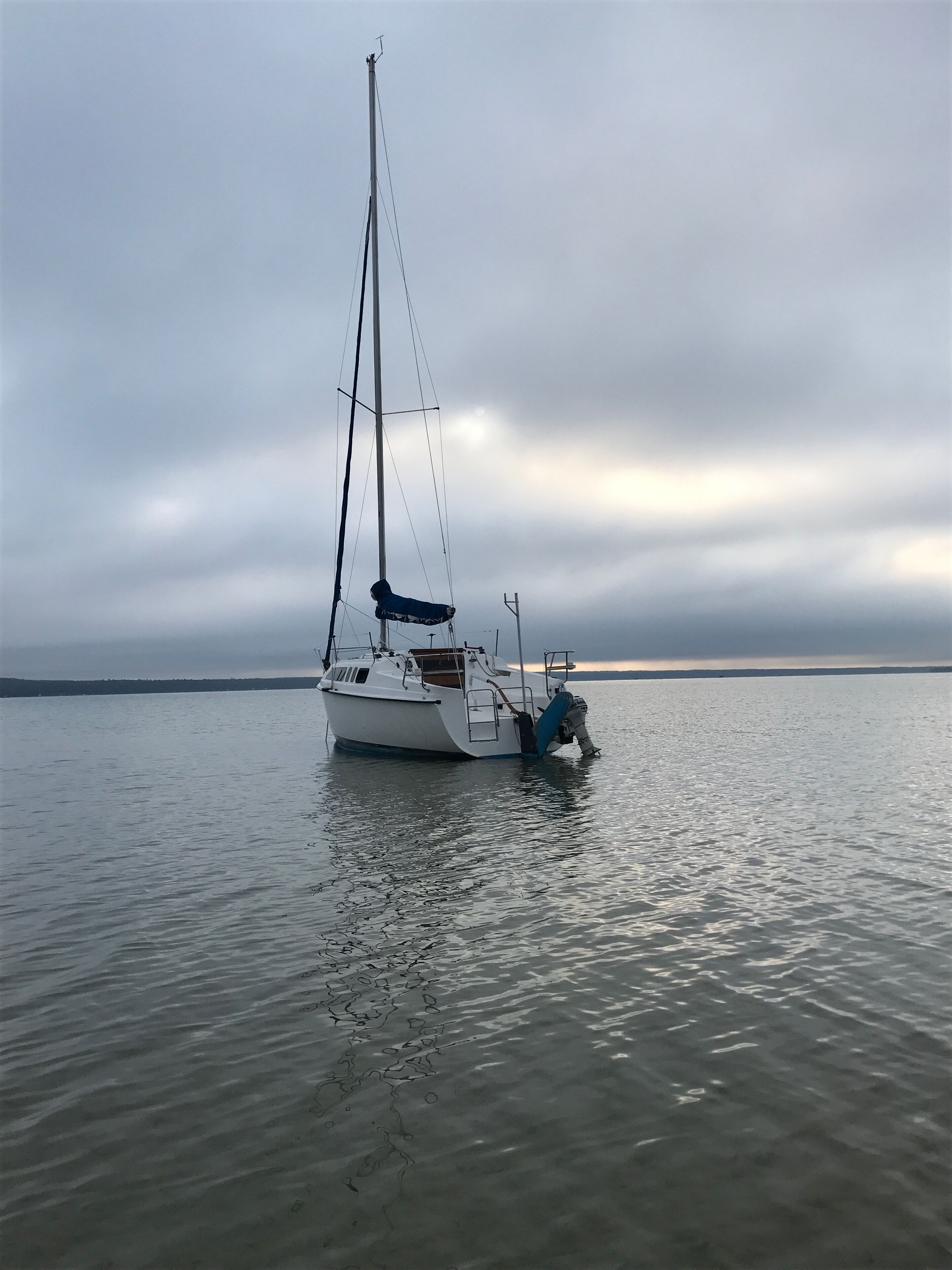 A sailboat anchored in calm waters with a cloudy sky in the background.