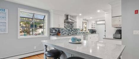 A modern kitchen with a large island, bar stools, and a view of the outdoors.