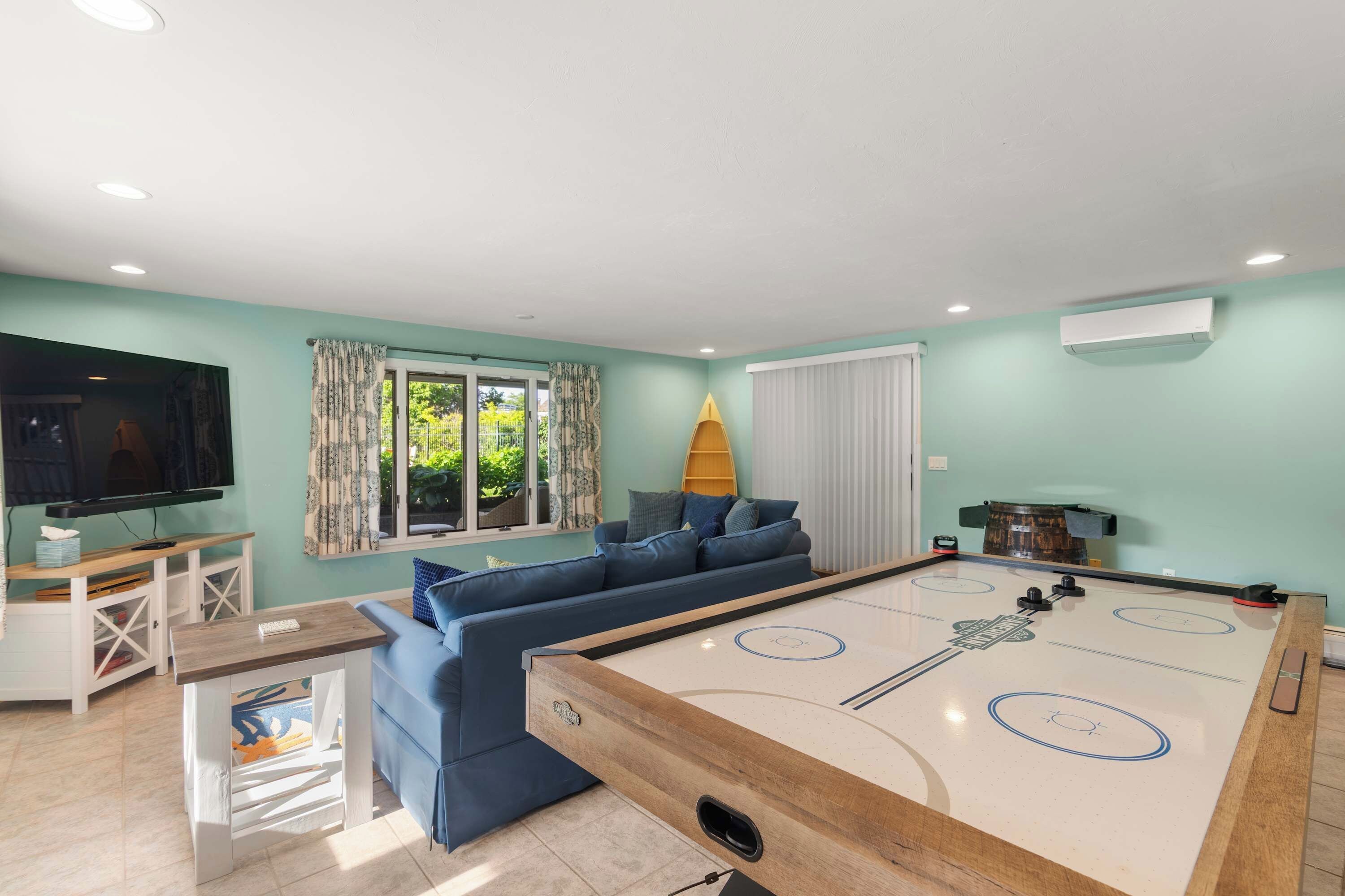 A living room with a pool table, a sofa, a television, and a window with curtains.