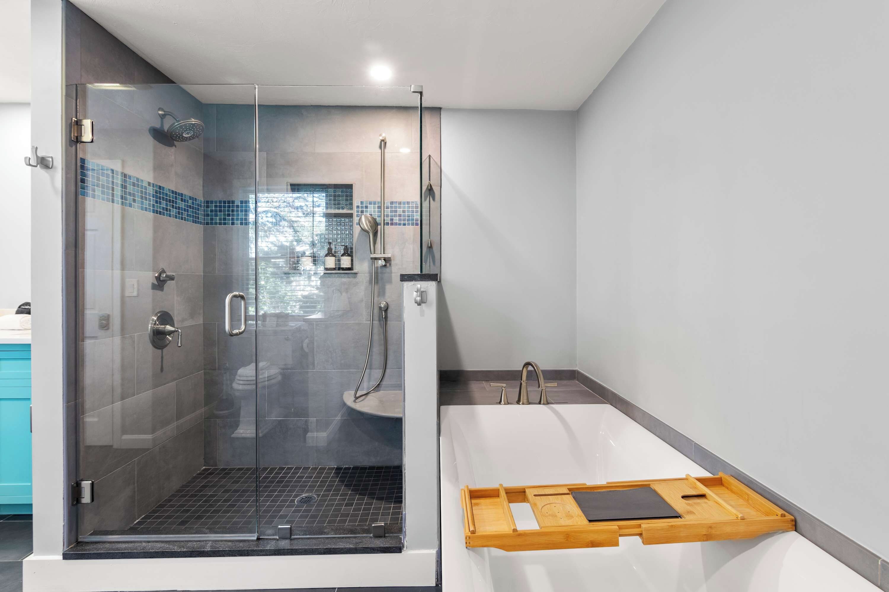 Un baño moderno con ducha de vidrio, una bañera blanca y una bandeja de madera.