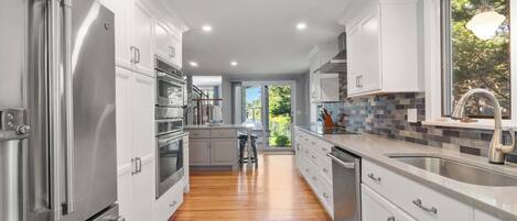 A modern kitchen with stainless steel appliances, white cabinetry, and a view to the outdoors.